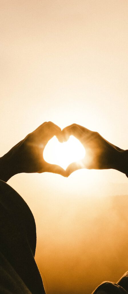 person doing heart shape hand with sun light passing thru